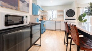 A modern kitchen with a microwave, stove, and sink. There are wooden cabinets and a dining area with a table and chairs. - Pet-Friendly St. Simons Island Beach Rental | The Blue Pearl (Saint Simons Island)