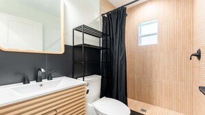 A modern bathroom with a white sink, black faucets, a white toilet, and a shower with a black curtain. - Pet-Friendly St. Simons Island Beach Rental | The Blue Pearl (Saint Simons Island)