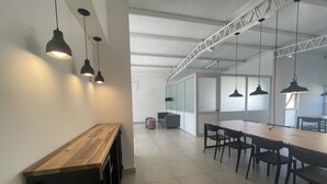 Un espace de bureau moderne avec une longue table en bois, des chaises noires et des luminaires suspendus.