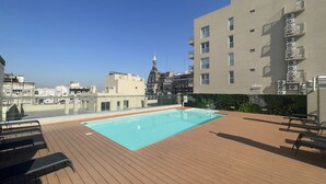 Un espace piscine aménag é sur le toit, avec une terrasse en bois, une piscine et une vue sur le paysage urbain.