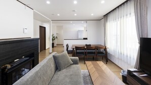 A modern living room with a sofa, a fireplace, a dining area with a table and chairs, and a TV. - COSMIC HILL (Sapporo)