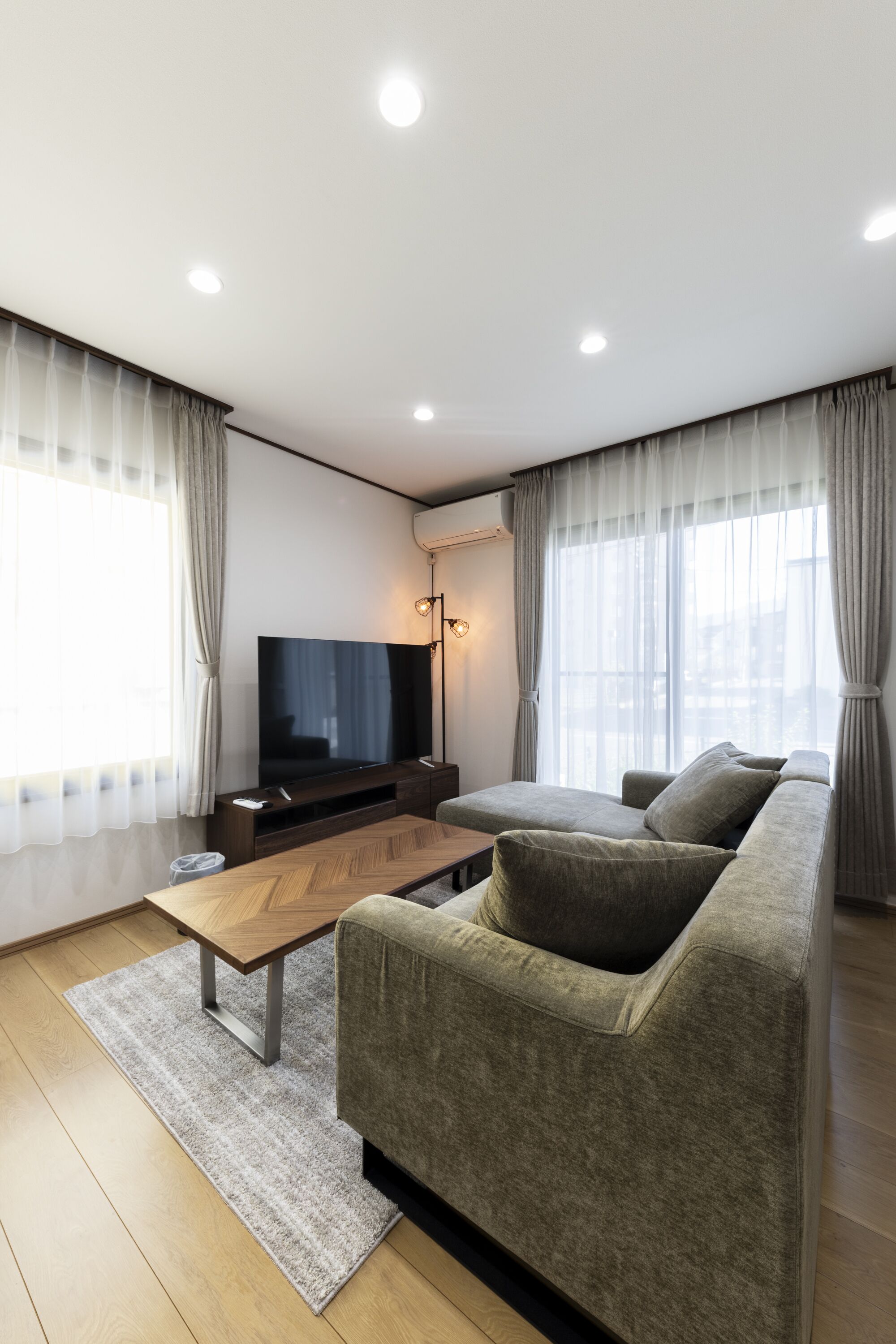 A modern living room with a flat-screen TV, a sofa, a coffee table, and a large window with curtains.