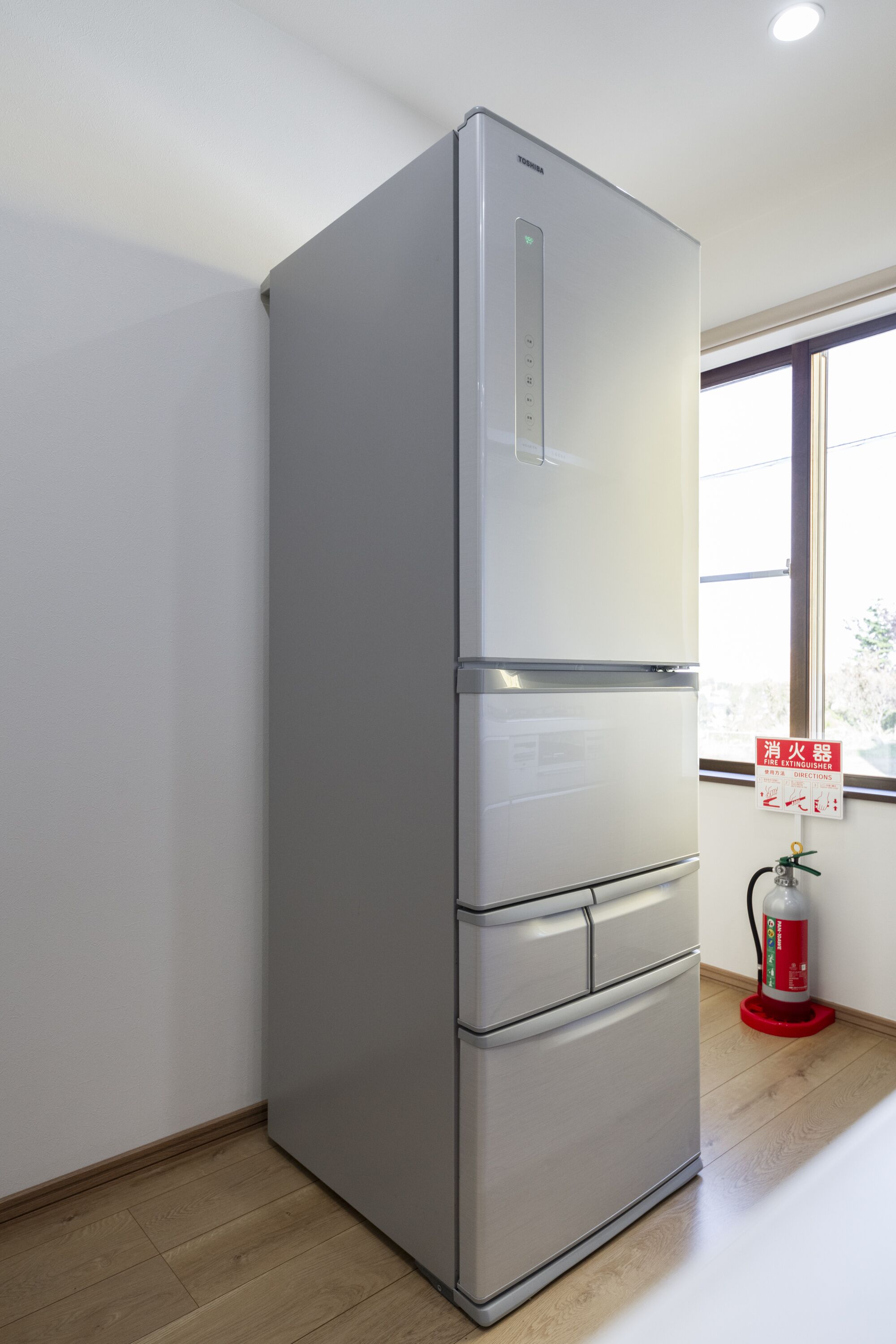 Eine moderne Küche mit einem Edelstahlkühlschrank, einem Fenster mit Blick und einem Feuerlöscher auf dem Boden.