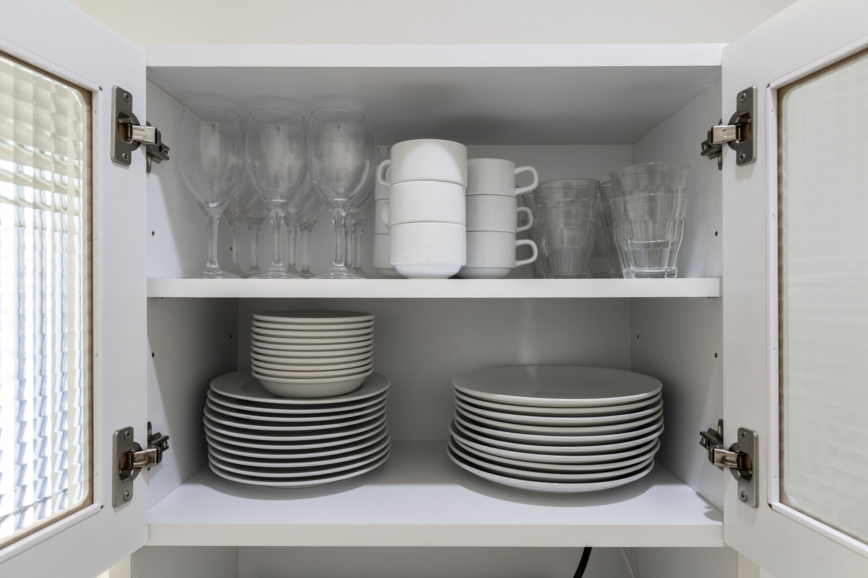A cabinet with shelves containing stacked plates and clear glassware.