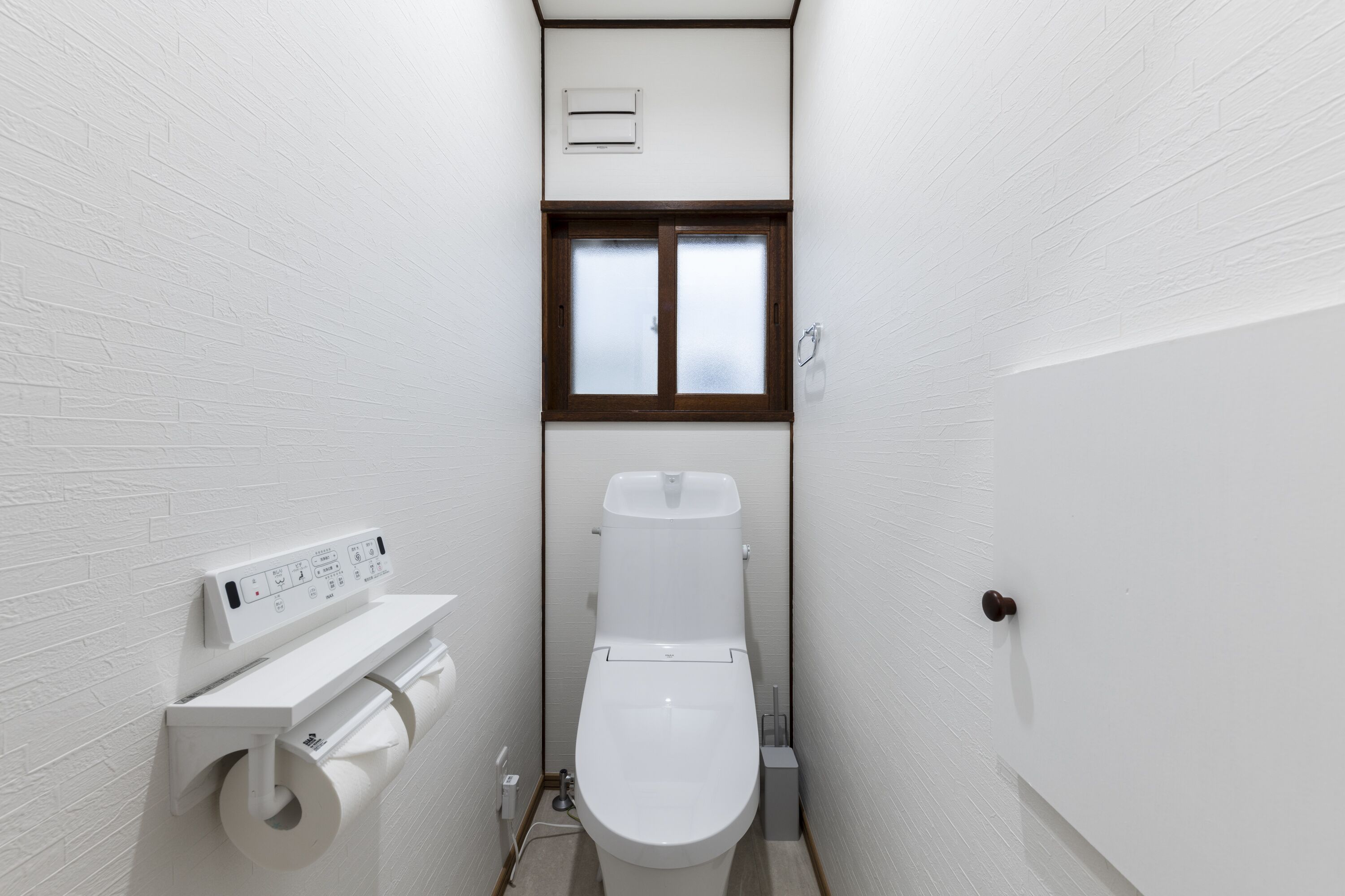 A small, narrow bathroom with a toilet, a window, and a wall-mounted toilet paper holder.