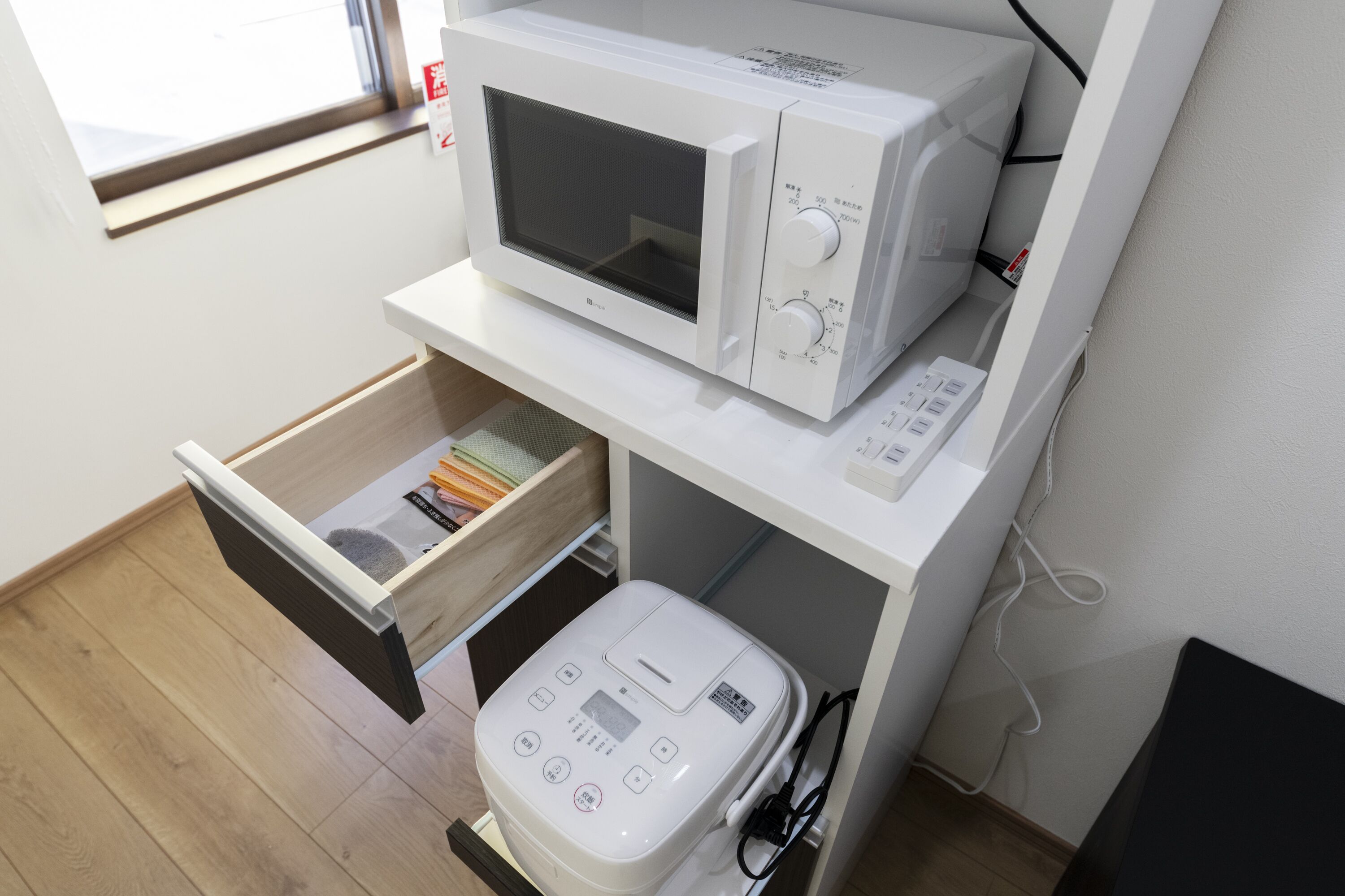 Una cocina compacta con microondas y cocedor de arroz sobre una encimera blanca.