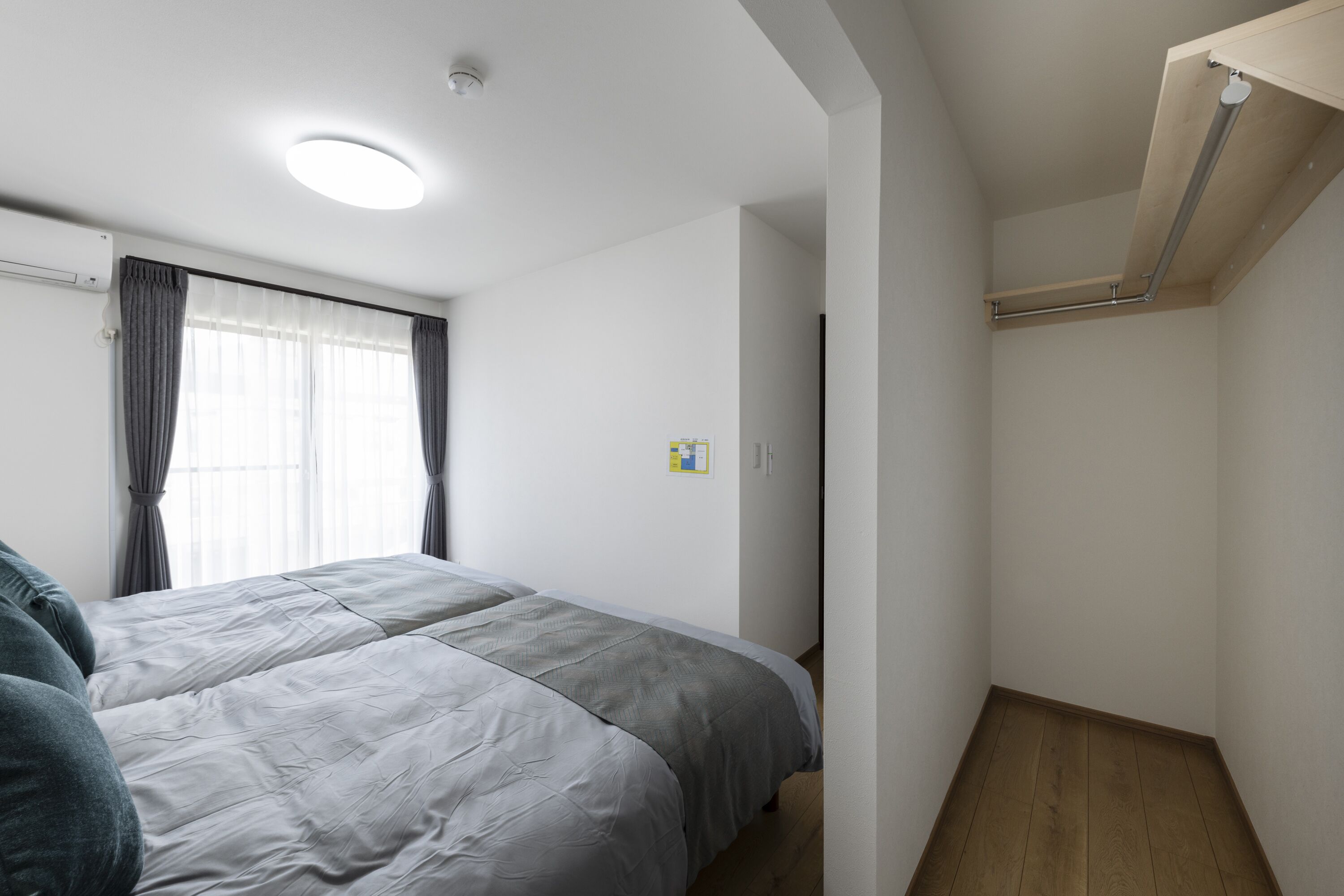 Une chambre à coucher avec un lit, une fenêtre avec des rideaux, un plancher en bois et un luminaire au plafond.