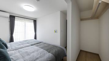 Une chambre à coucher avec un lit, une fenêtre avec des rideaux, un plancher en bois et un luminaire au plafond.