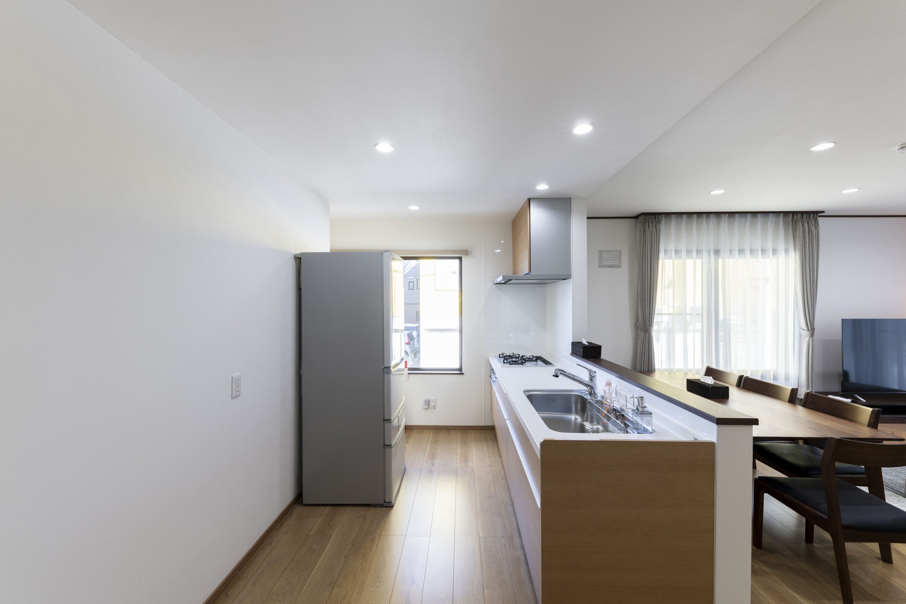 A modern kitchen with a central island, a dining area with a table and chairs, and a large window with curtains.