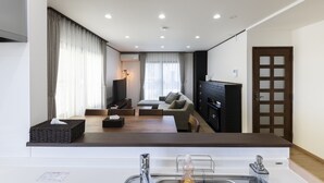 A modern living room with a sofa, a TV, and a fireplace. There is a dining area with a table and chairs. - COSMIC HILL (Sapporo)