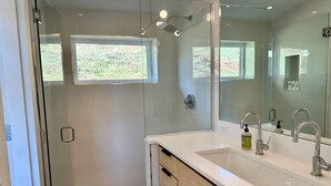 Un baño moderno con cabina de ducha de vidrio, un espejo grande y un lavamanos blanco con dos grifos.