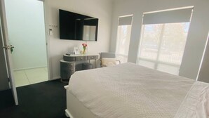 Une chambre d’hôtel dotée d’un grand lit, d’un téléviseur à écran plat fixé au mur, d’un petit bureau avec une chaise et d’une fenêtre donnant sur l’extérieur.