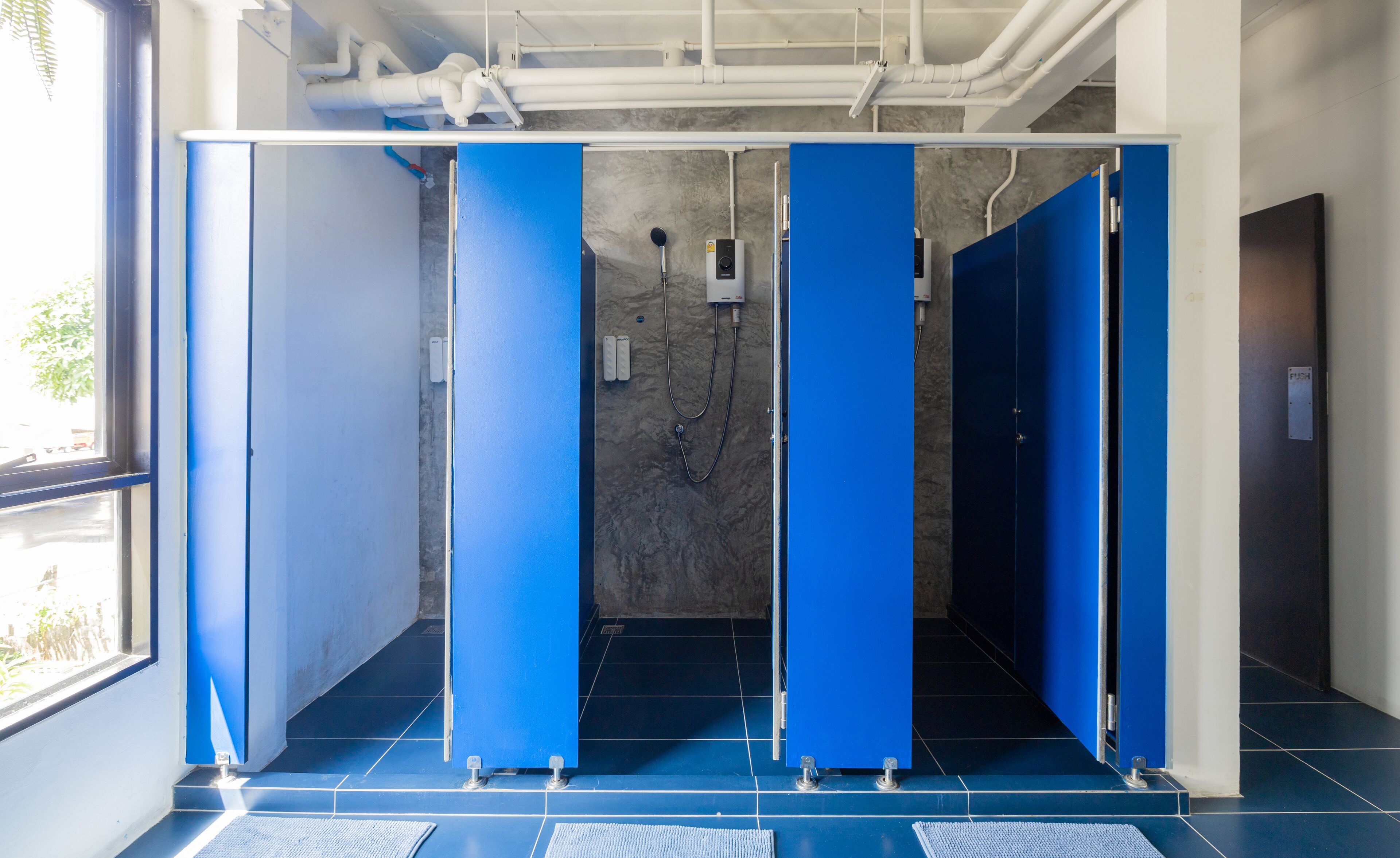 A public restroom with blue stalls, a hand dryer, and a water fountain.