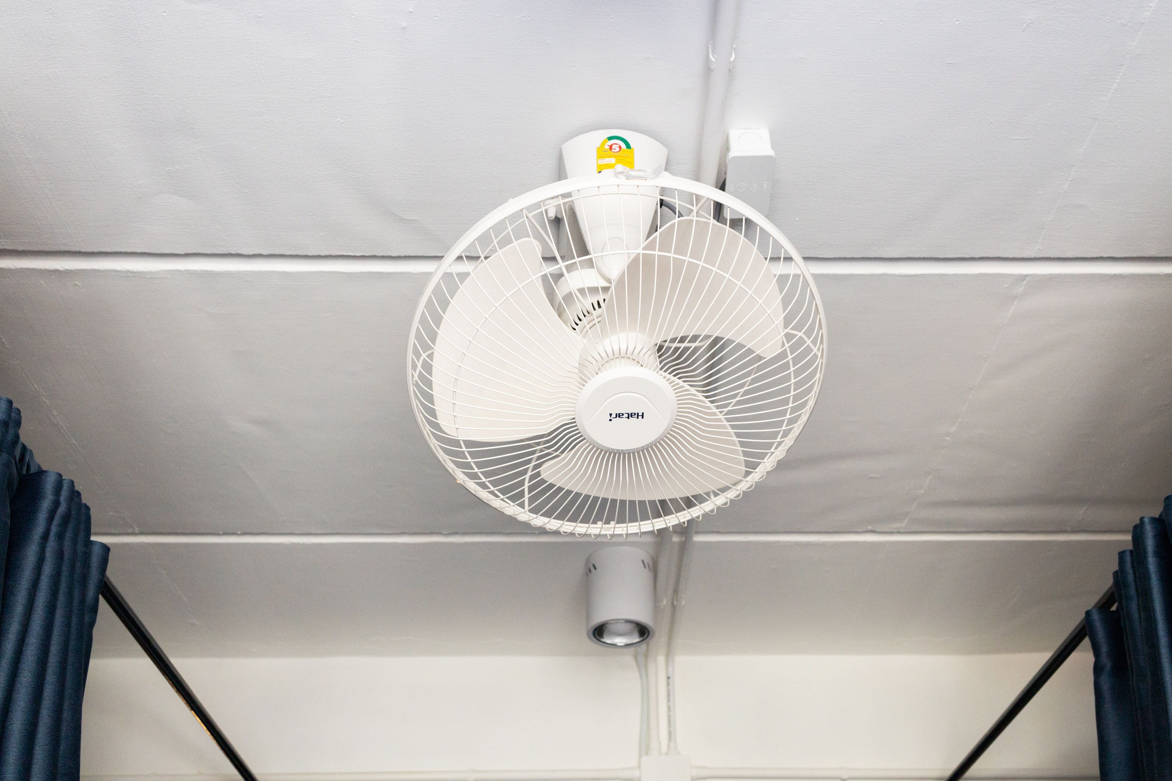 Ventilador branco fixado no teto, com painel de controle e alojamento de motor cilíndrico.