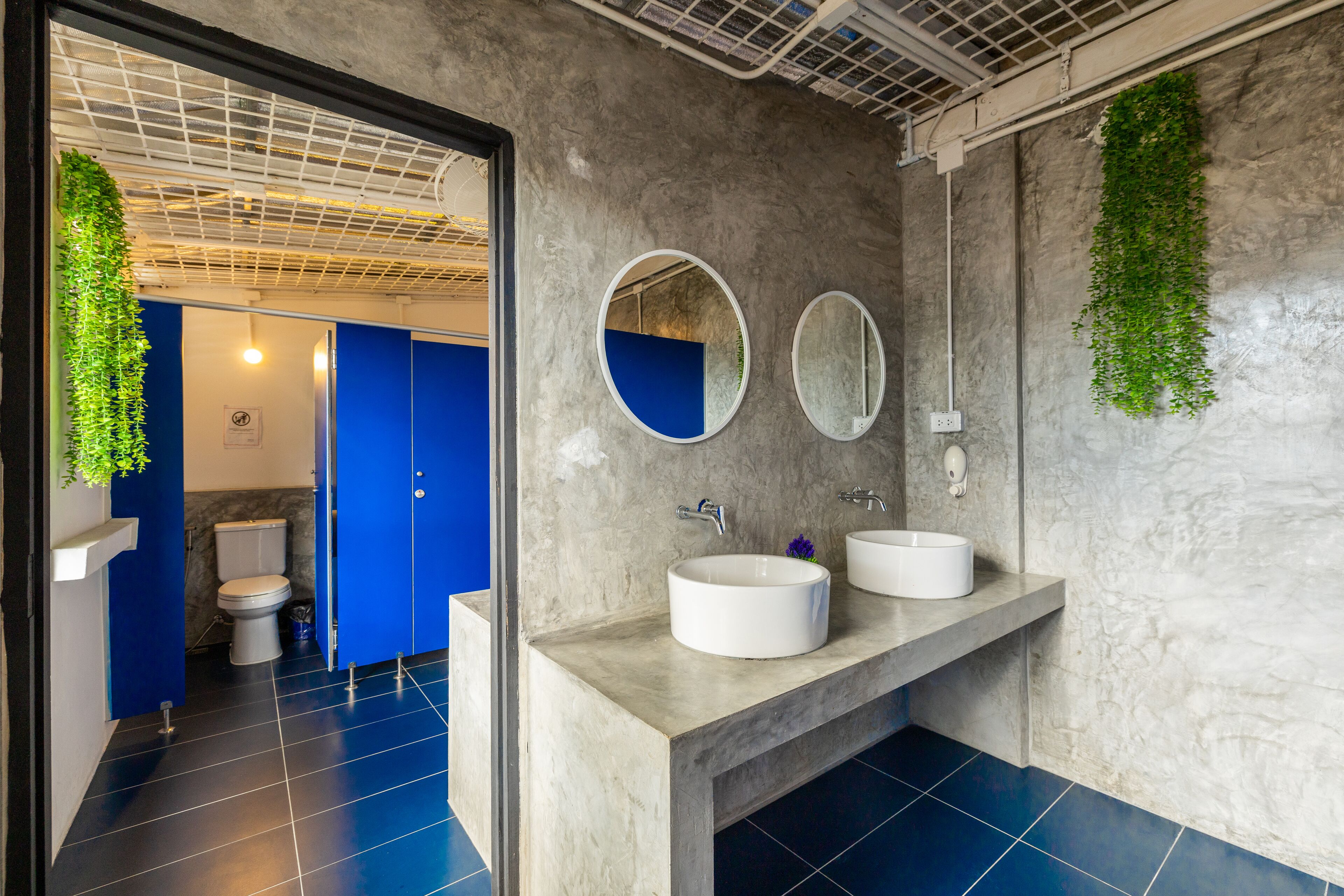 A modern bathroom with two white sinks, a blue toilet, and a mirror.