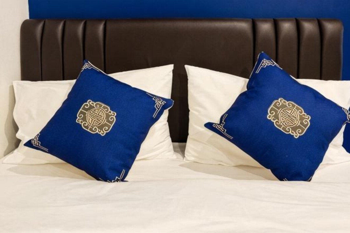 Una cama con dos almohadas azules y una blanca, cabecera oscura y pared azul.