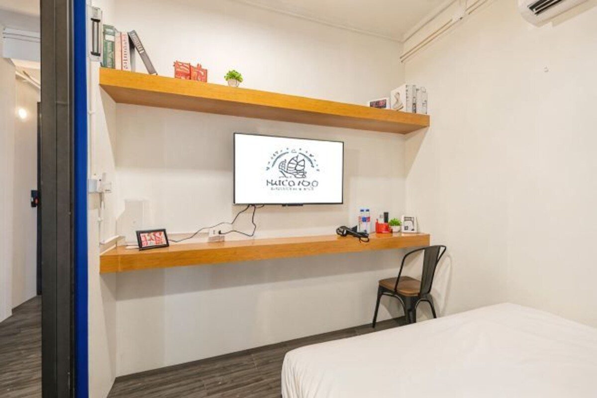 Habitación de hotel con una cama, un escritorio con computadora, una silla y un televisor fijado a la pared.