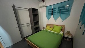 A bedroom with a bed, a wardrobe, a nightstand, and a window with curtains. - Havre de Paix - Bungalow de Charme (Baie-Mahault)