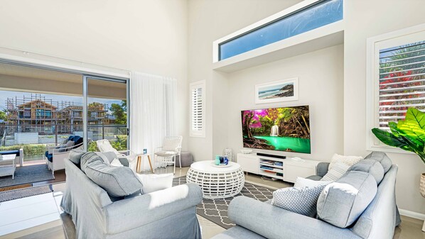 A modern living room with a large TV, comfortable seating, and a view of a construction site.