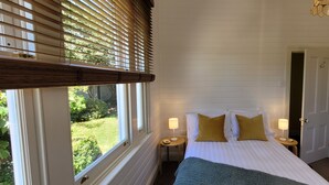 A bedroom with a bed, two bedside tables, a nightstand, a window with blinds, and a door.