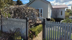 A house with a white fence, a garden with various plants, and a clear blue sky.