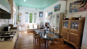 A kitchen with a gas stove, wooden cabinets, a dining table with chairs, and a window with a view of greenery.