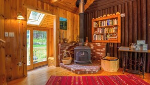 A cozy cabin interior with a wood-burning stove, a bookshelf, and a skylight. - Meerman Camp - PRIVATE Rangeley Lake waterfront cottage, with a small beach! (Rangeley)