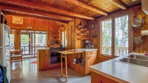 A wooden cabin kitchen with a wooden table, stove, and large windows. - Meerman Camp - PRIVATE Rangeley Lake waterfront cottage, with a small beach! (Rangeley)