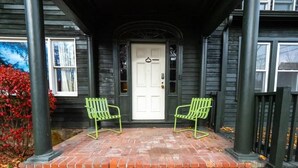 Un portico con due sedie verdi, una porta bianca e un vialetto in mattoni.