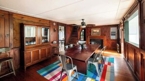 Una sala da pranzo in legno con un tavolo grande e sedie, un tappeto colorato e una scala che conduce a un altro piano.