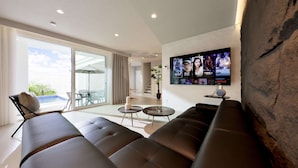 A modern living room with a large flat-screen TV mounted on the wall, a sofa, a coffee table, and a dining area with a table and chairs. - Crystal Villa SHIRARAHAMA BEACH (Shirahama)