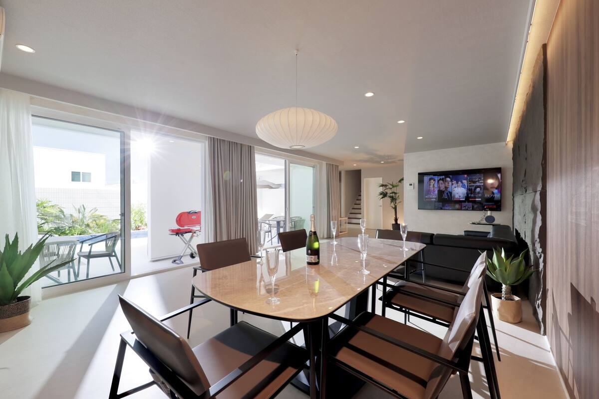Un espace repas moderne avec une grande table, des chaises et un téléviseur fixé au mur.