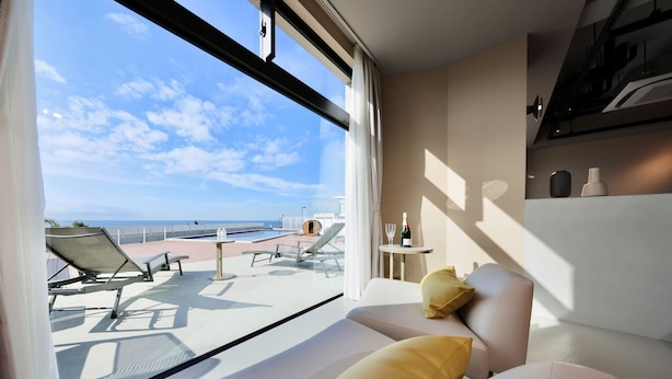 A modern room with a view of the sea, a balcony with sun loungers, and a small table with a bottle and glasses. - Crystal Villa SHIRARAHAMA BEACH (Shirahama)