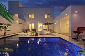 Uma área de piscina moderna com hidromassagem, espreguiçadeiras e churrasqueira.
