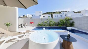 A rooftop pool area with a hot tub, lounge chairs, and a table with a bottle and glass.
