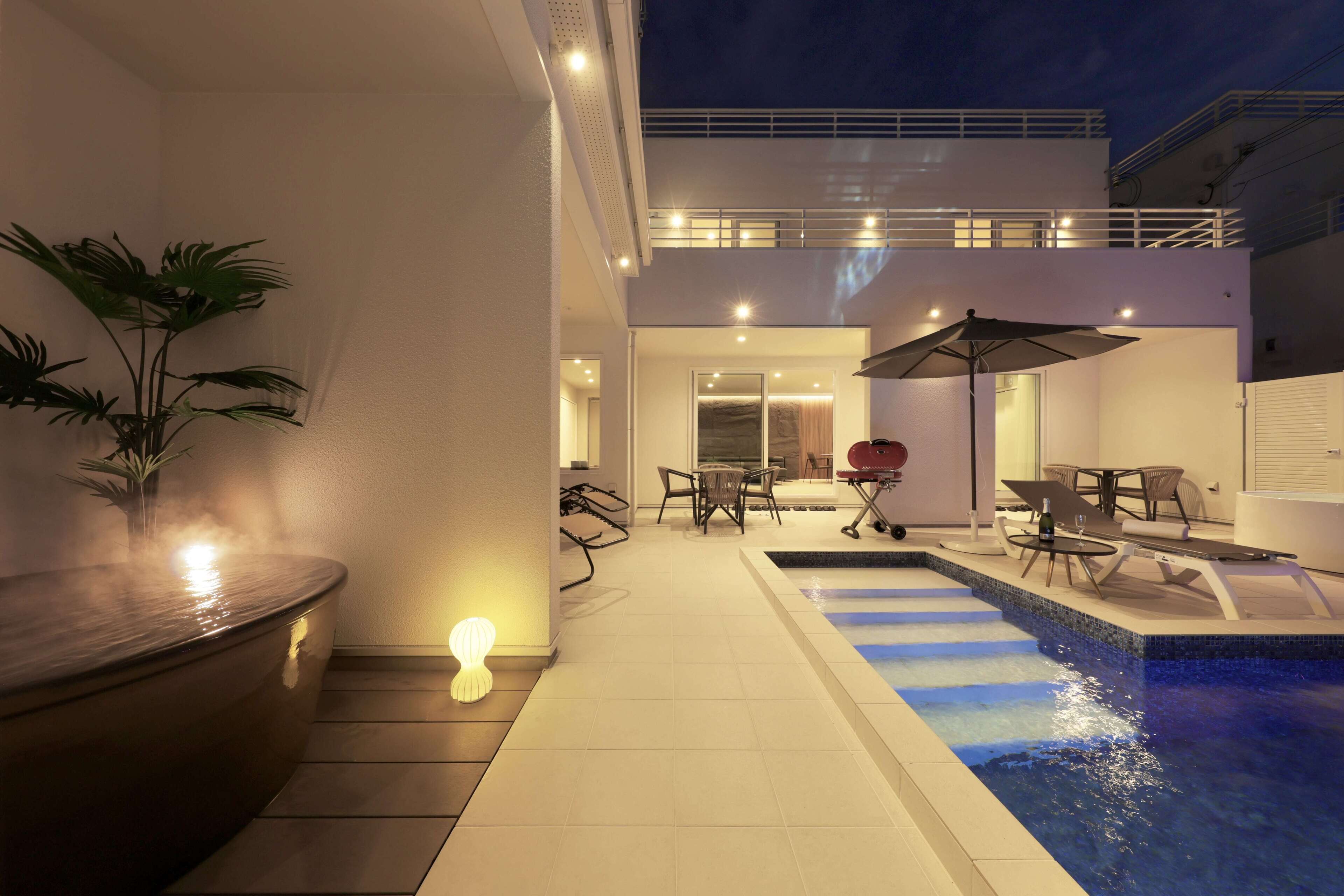 A modern outdoor pool area with a hot tub, lounge chairs, and a dining table with umbrellas.