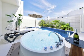 Uma banheira de hidromassagem com uma garrafa e taça de champanhe, cercada por plantas e uma piscina.