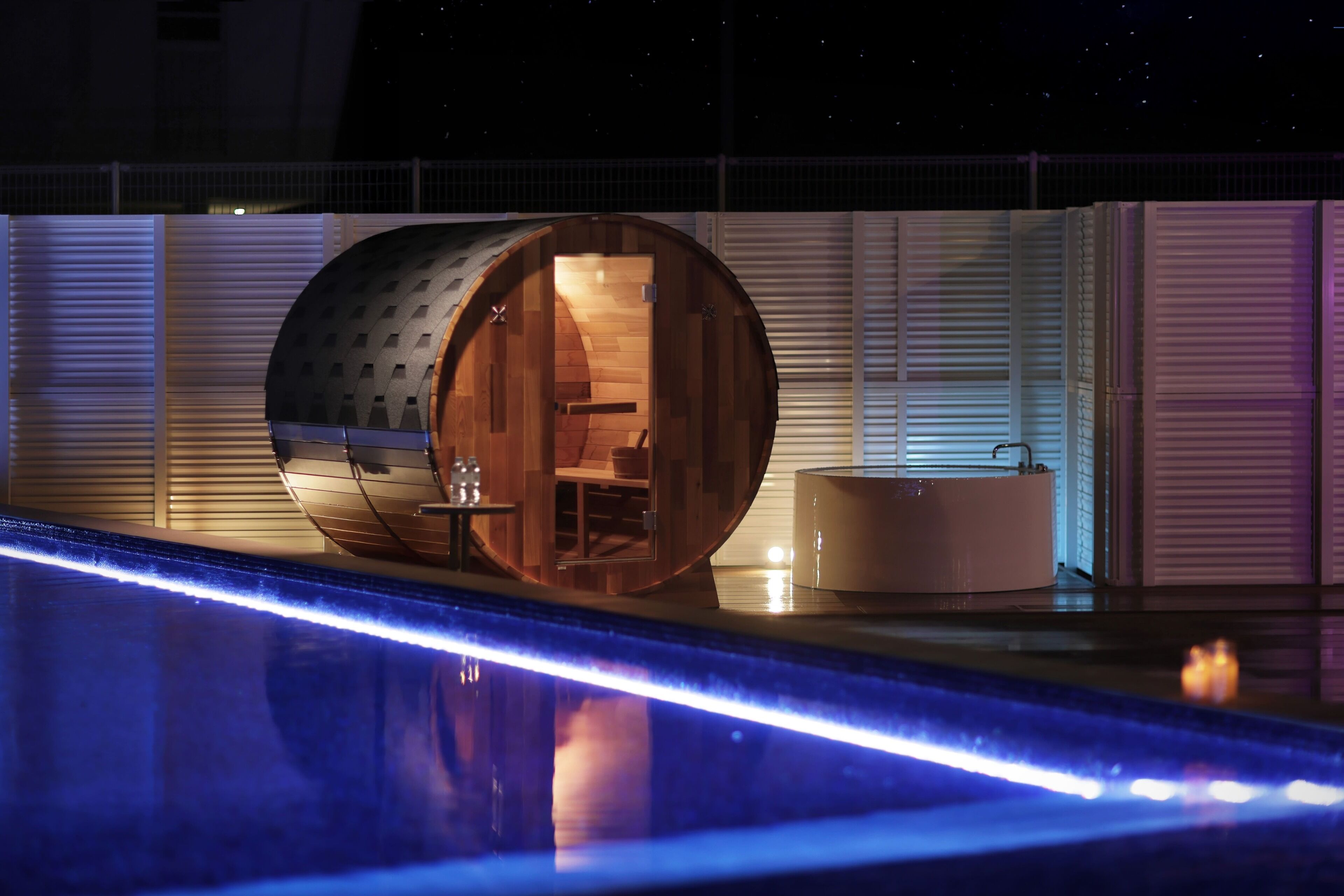 Una habitación moderna y cilíndrica con interior de madera, una bañera y una zona junto a la piscina con iluminación azul.