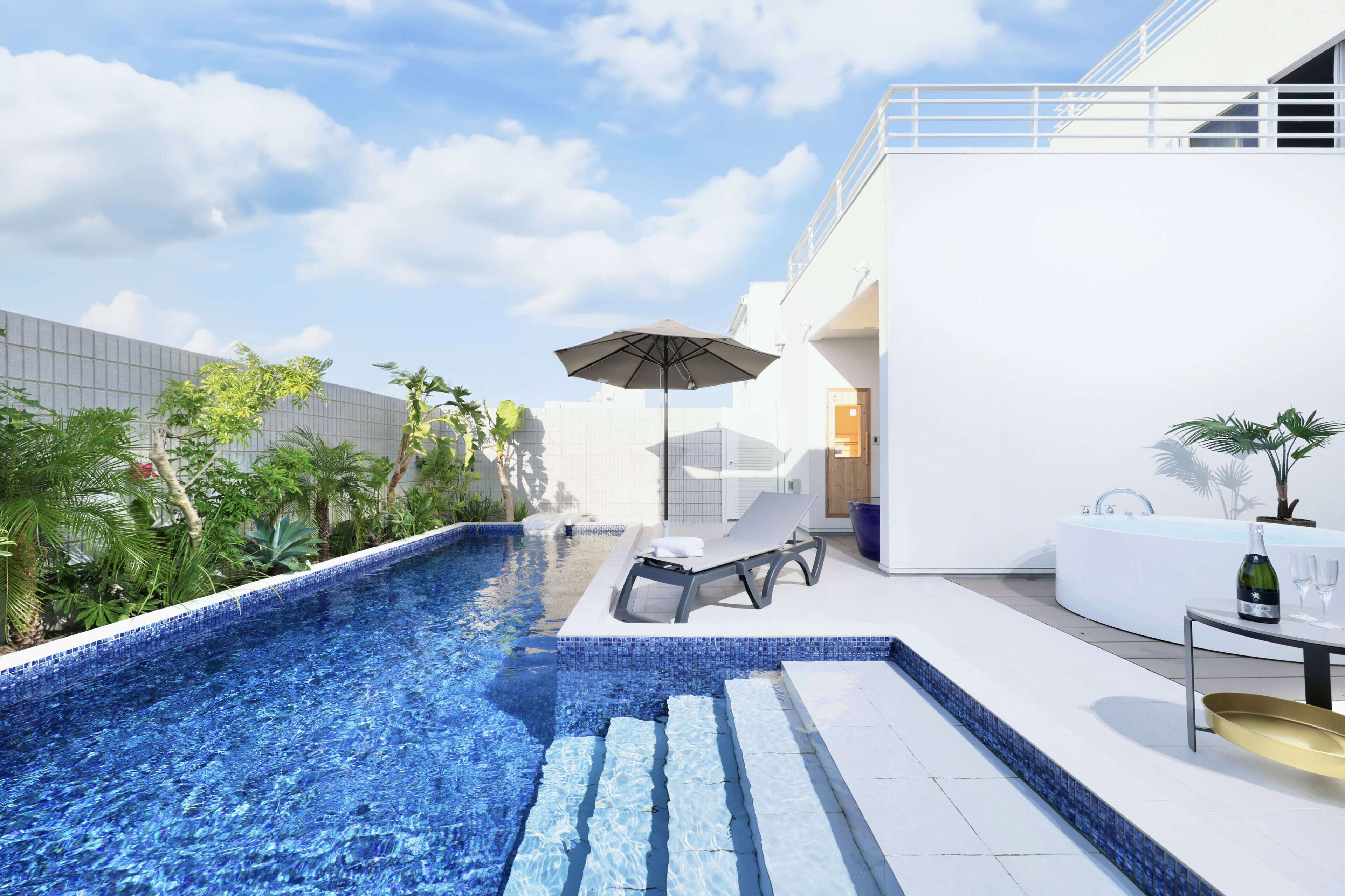 Un espace piscine extérieur moderne, doté d’une chaise longue, d’un parasol et d’une table avec une bouteille et un verre.