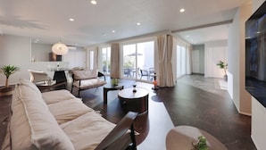 A spacious living area with a sofa, coffee table, and dining table. There is a large window with curtains, a TV, and a plant. - Crystal Villa SHIRARAHAMA BEACH (Shirahama)