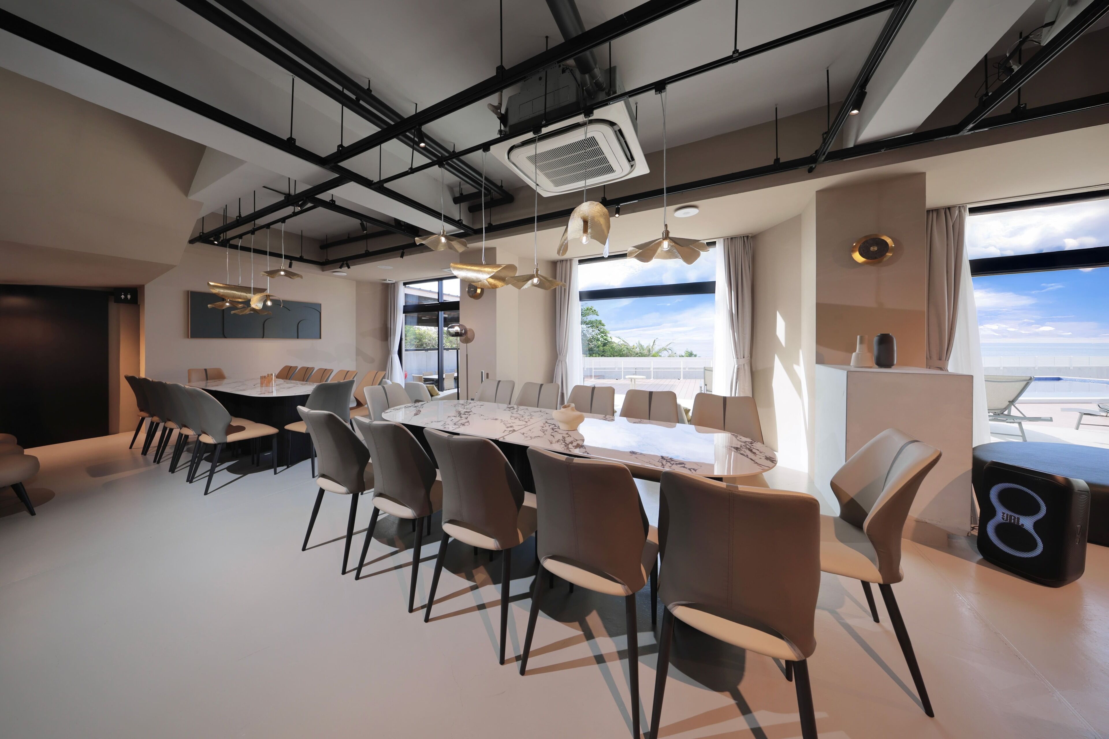 Un comedor moderno con una gran mesa ovalada, múltiples sillas, iluminación colgante y vistas al exterior a través de amplias ventanas.