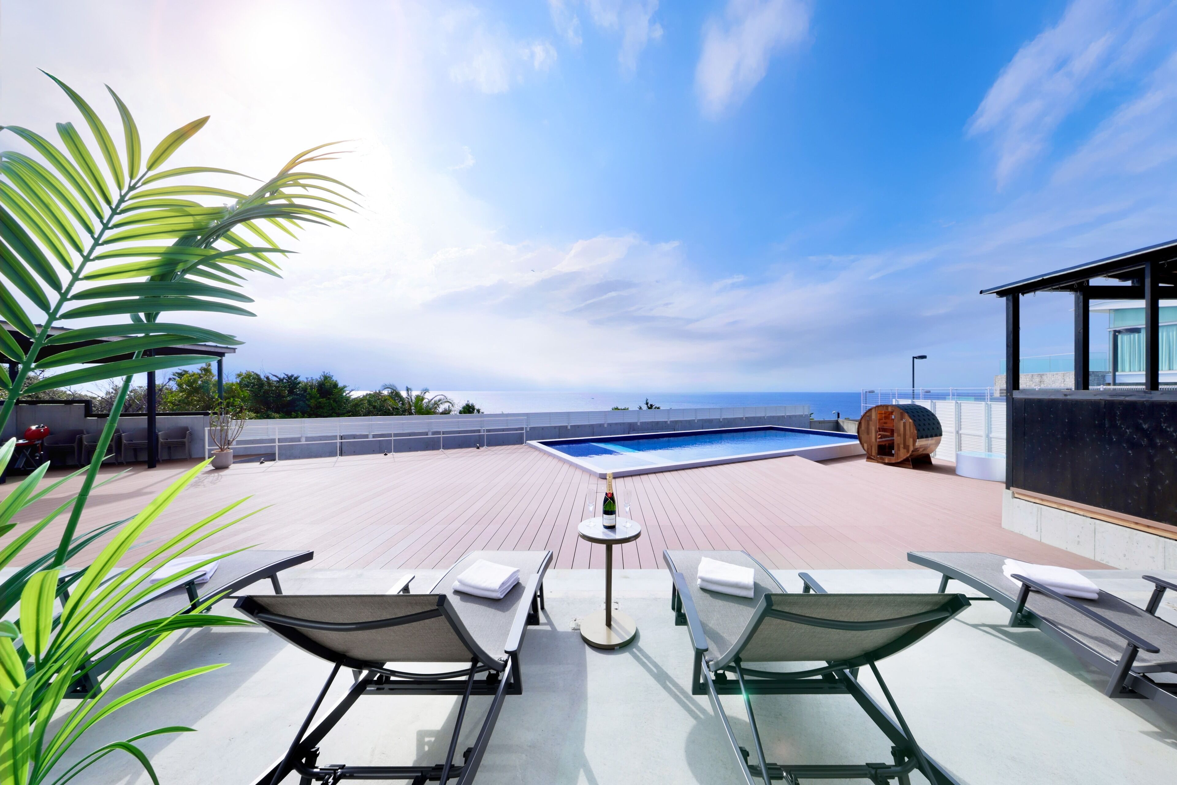 A rooftop pool area with lounge chairs, a small table with a bottle, and a view of the ocean.