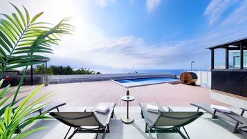 A rooftop pool area with lounge chairs, a small table with a bottle, and a view of the ocean.