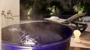 A spa area with a large blue bathtub, a lounge chair, and a small white candle.