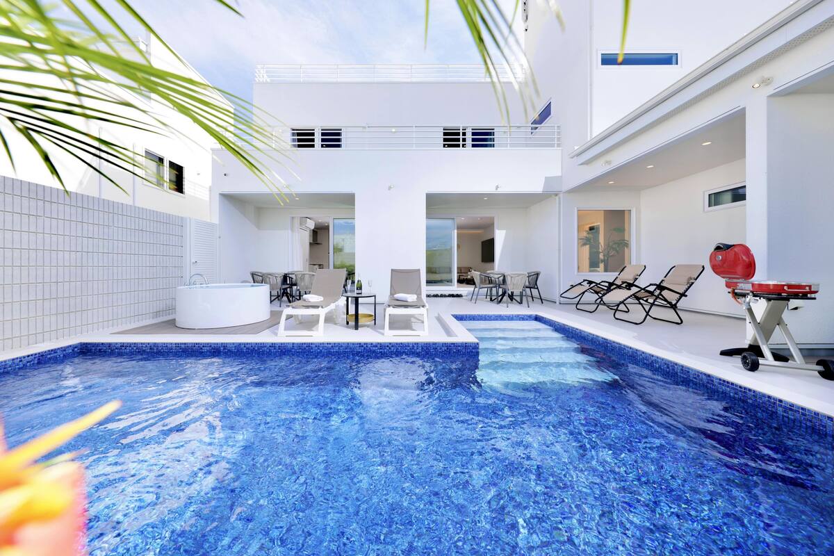 Un espace piscine intérieur moderne comprenant deux bassins distincts, des chaises longues et un jacuzzi.