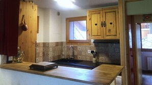 Een keuken met houten kastjes, een raam en een betegelde achterwand.