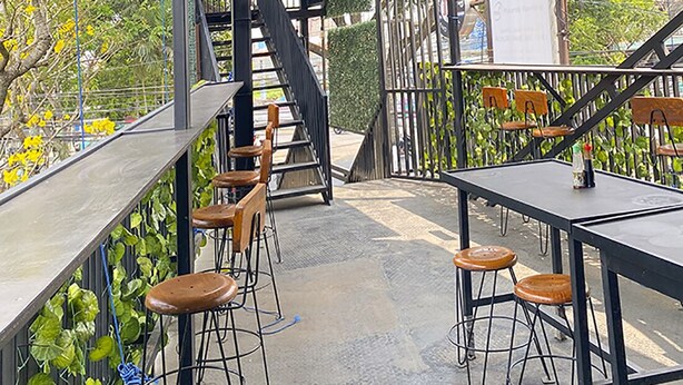 Un espacio al aire libre con mesas y sillas, una escalera y vistas a árboles y edificios.