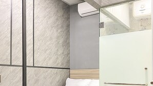 Un dormitorio moderno con cama, mesita de noche, separador de vidrio y unidad de aire acondicionado.