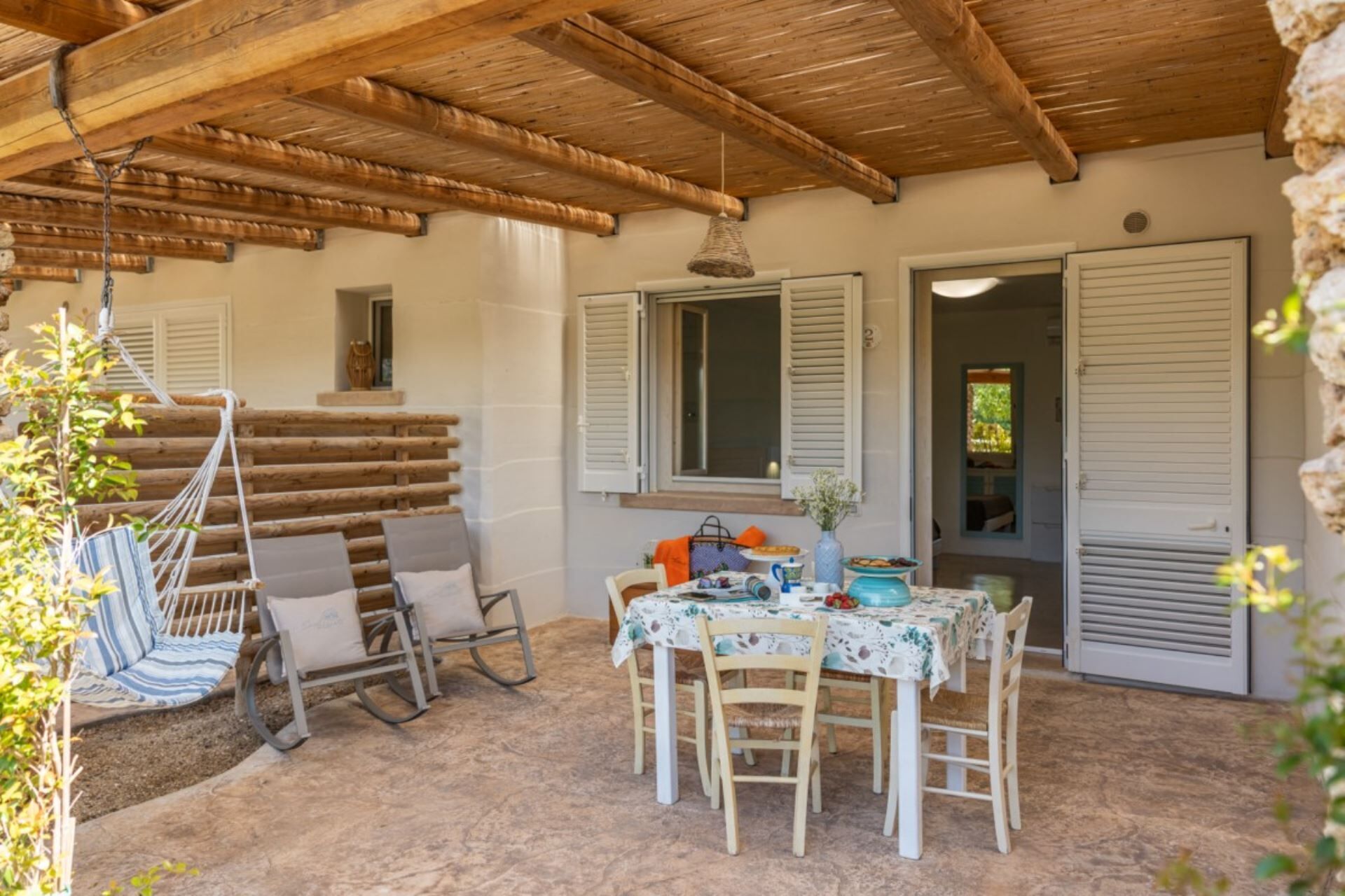 Un espace extérieur abrité, aménagé avec une table et des chaises, un hamac et offrant une vue sur l’intérieur.