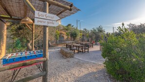 An outdoor seating area with tables and chairs, a foosball table, and a sign reading "barbecue parco giochi". - Cava Li Santi Residence - Monolocale Family Int 2 (Santa Caterina)